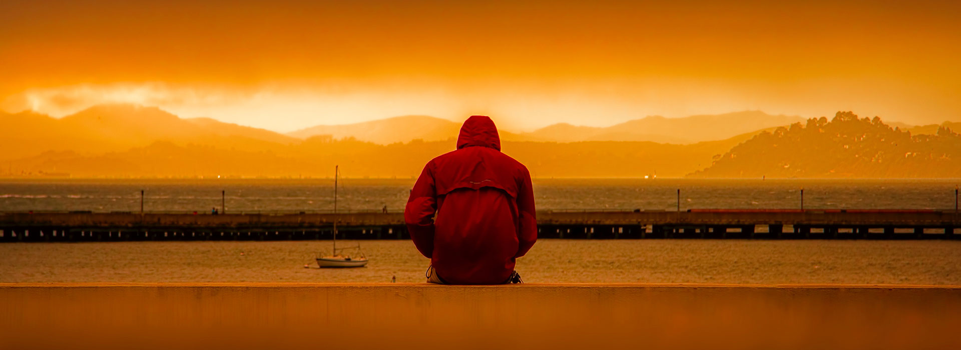 A person wearing a hoodie facing into a sunset.