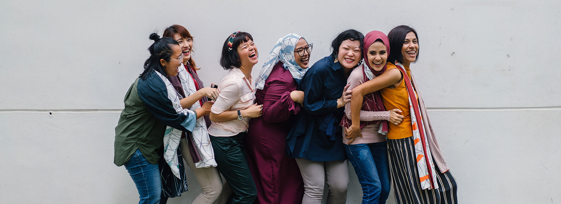 A group of culturally diverse women candidly hugging and laughing.