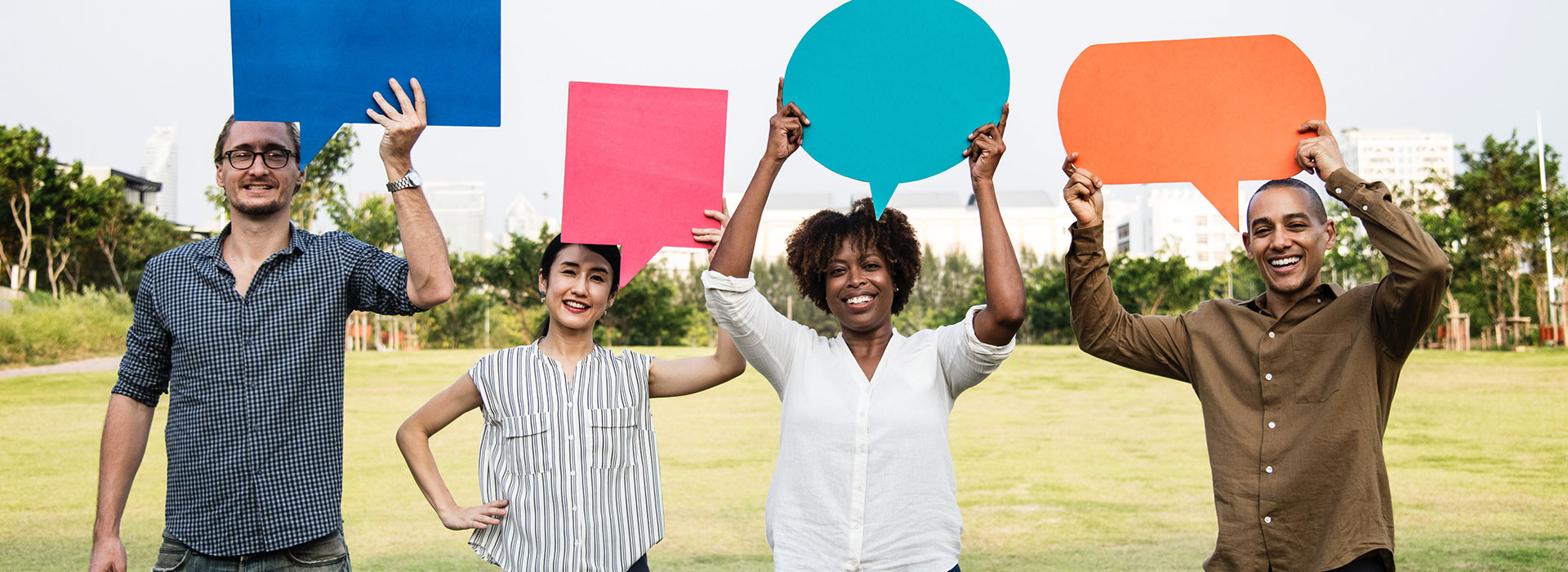 Four diverse individuals standing next to each other, smiling and holding coloured speech bubbles above their heads.