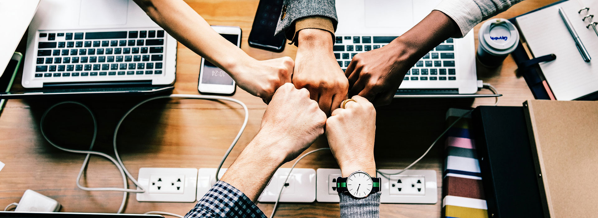 Five people fist bumping over laptops and notebooks.