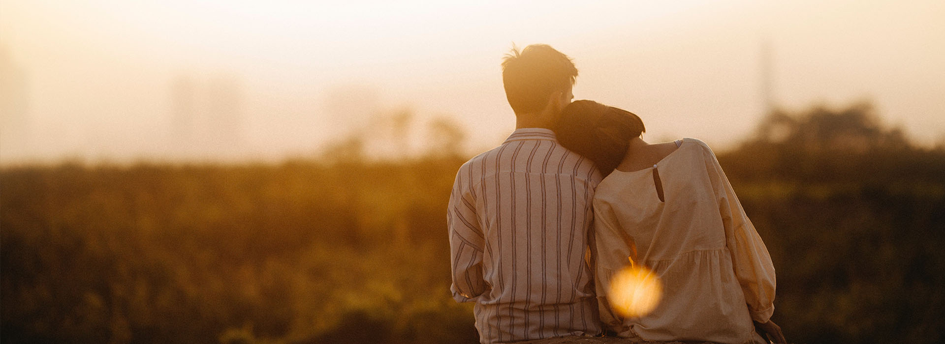A female resting her head on a male's shoulder while watching a sunset.