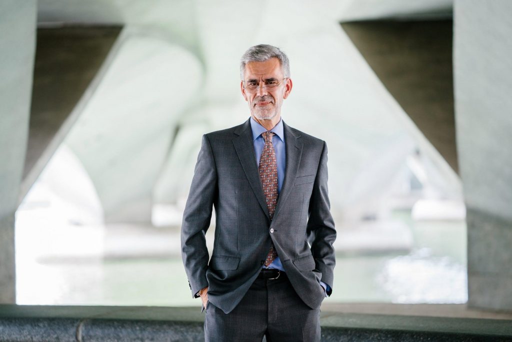 Older man in grey suit in front of industrial background