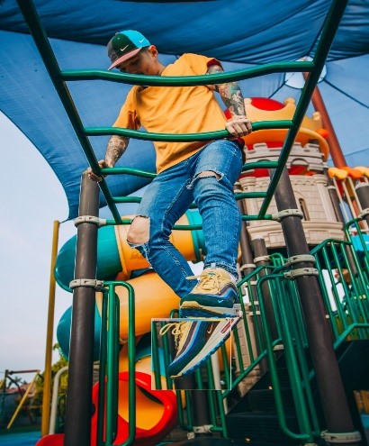 young man in yellow tshirt and jeans on monkey bars in playground