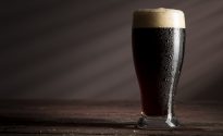 Back in black: brewing stouts Wet glass of cold dark beer with foam placed on a rustic wooden table.
