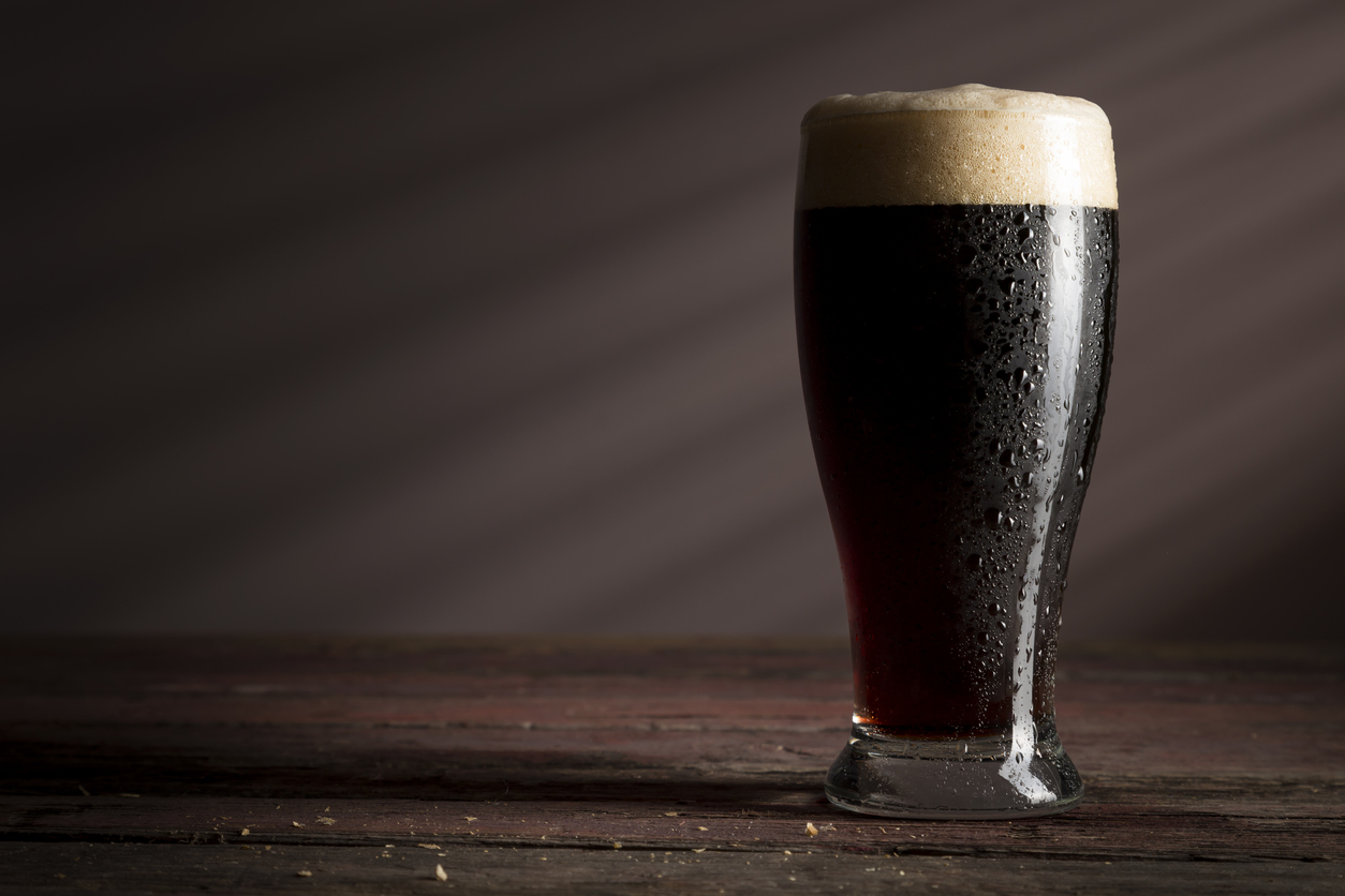 Back in black: brewing stouts Wet glass of cold dark beer with foam placed on a rustic wooden table.
